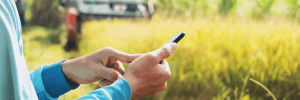 farmer using a smartphone, standing in a field in front of a tractor